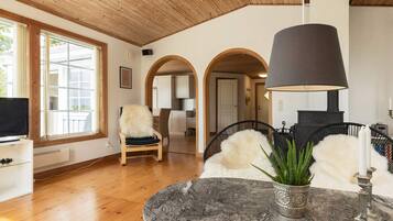 Una sala de estar moderna con techo de madera, chimenea de piedra y vista a la cocina a través de un arco.