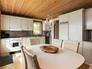 A kitchen with white cabinets, a stove, and a dining table with chairs. - 7 Person Holiday Home in Svendborg (Svendborg)