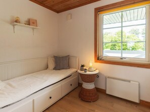 A small, cozy room with a single bed, a bedside table with a lamp, a radiator, and a window with a view of greenery. - 7 Person Holiday Home in Svendborg (Svendborg)