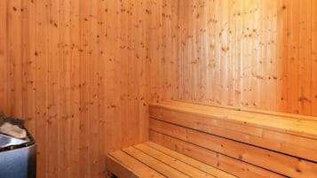 Una sauna con bancos de madera y un recipiente metálico, probablemente para agua o vapor.