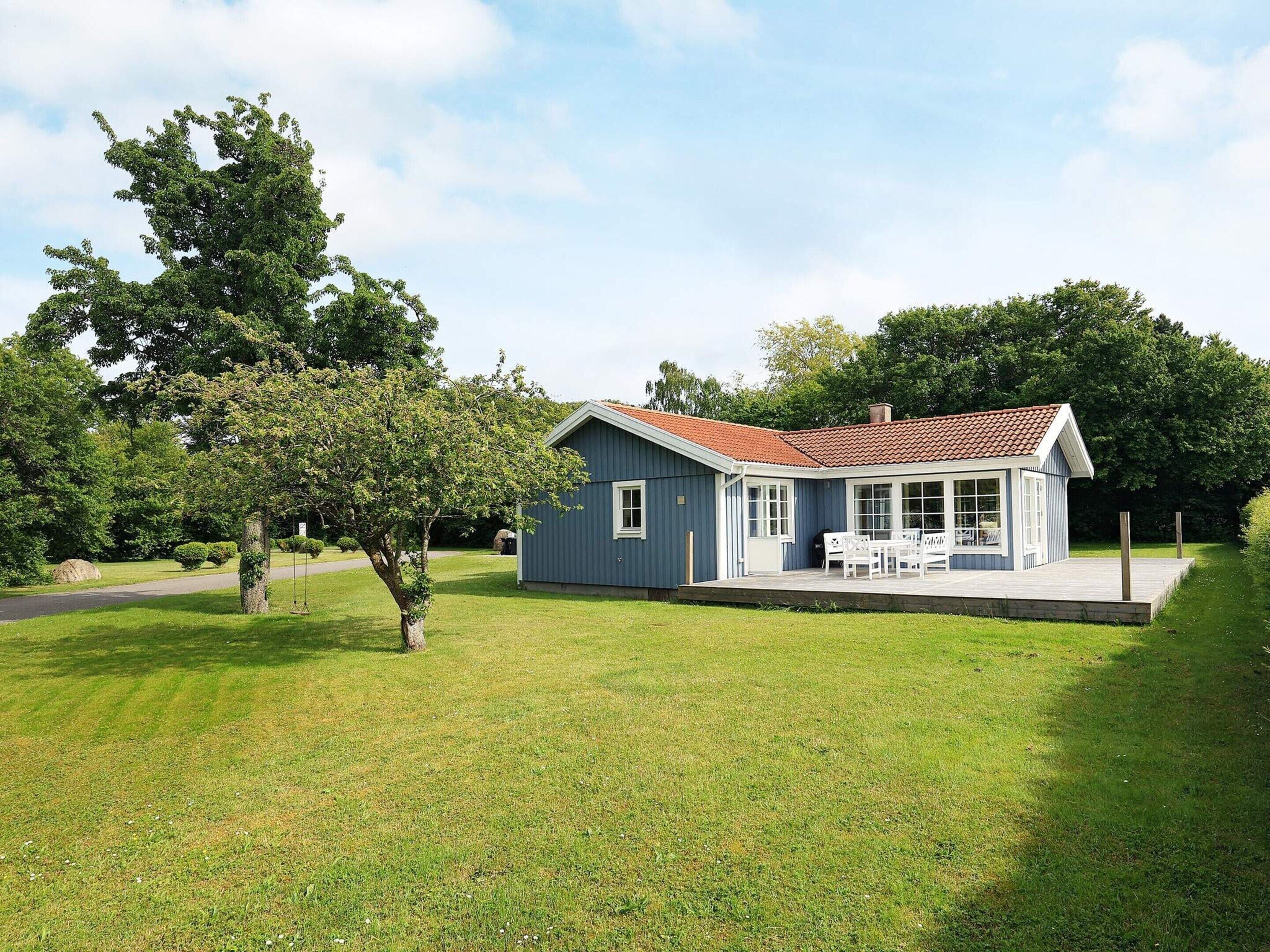 A single-story house with a red-tiled roof, a porch with white furniture, and a well-maintained lawn.