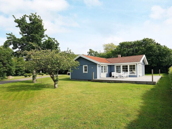 A single-story house with a red-tiled roof, a porch with white furniture, and a well-maintained lawn.