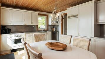 A modern kitchen with white cabinetry, a round dining table, wicker chairs, and a chandelier.
