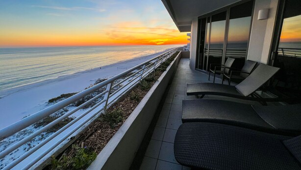 A balcony with a view of the beach and ocean during sunset.