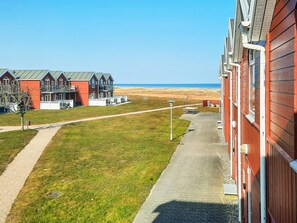 A coastal hotel with a paved walkway leading to the beach, featuring multiple red buildings with balconies.