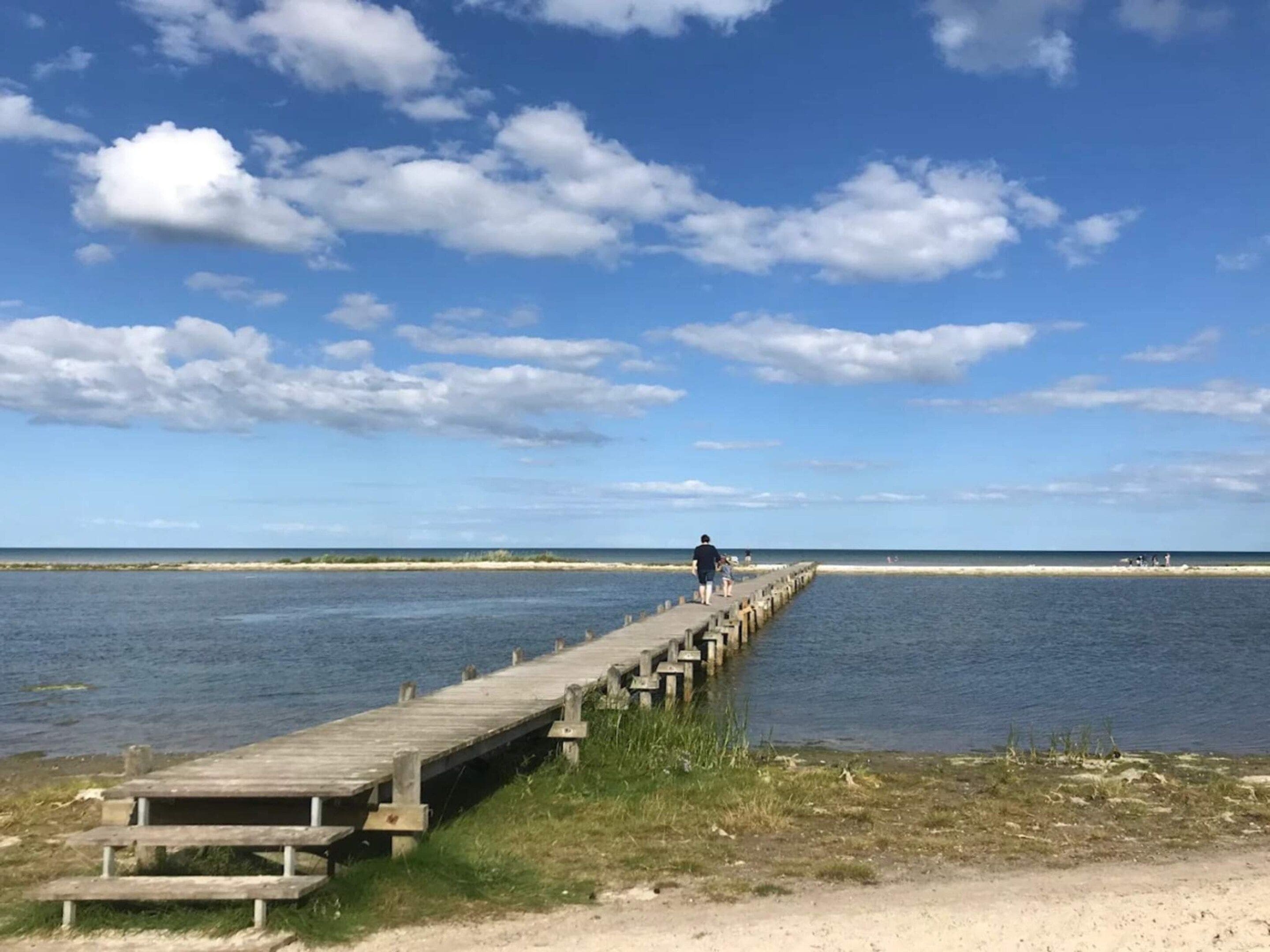A wooden pier extending into calm waters with a clear sky above.