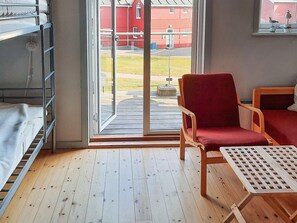 A room with a bunk bed, a red chair, a wooden table, and a sliding glass door leading to an outdoor area.