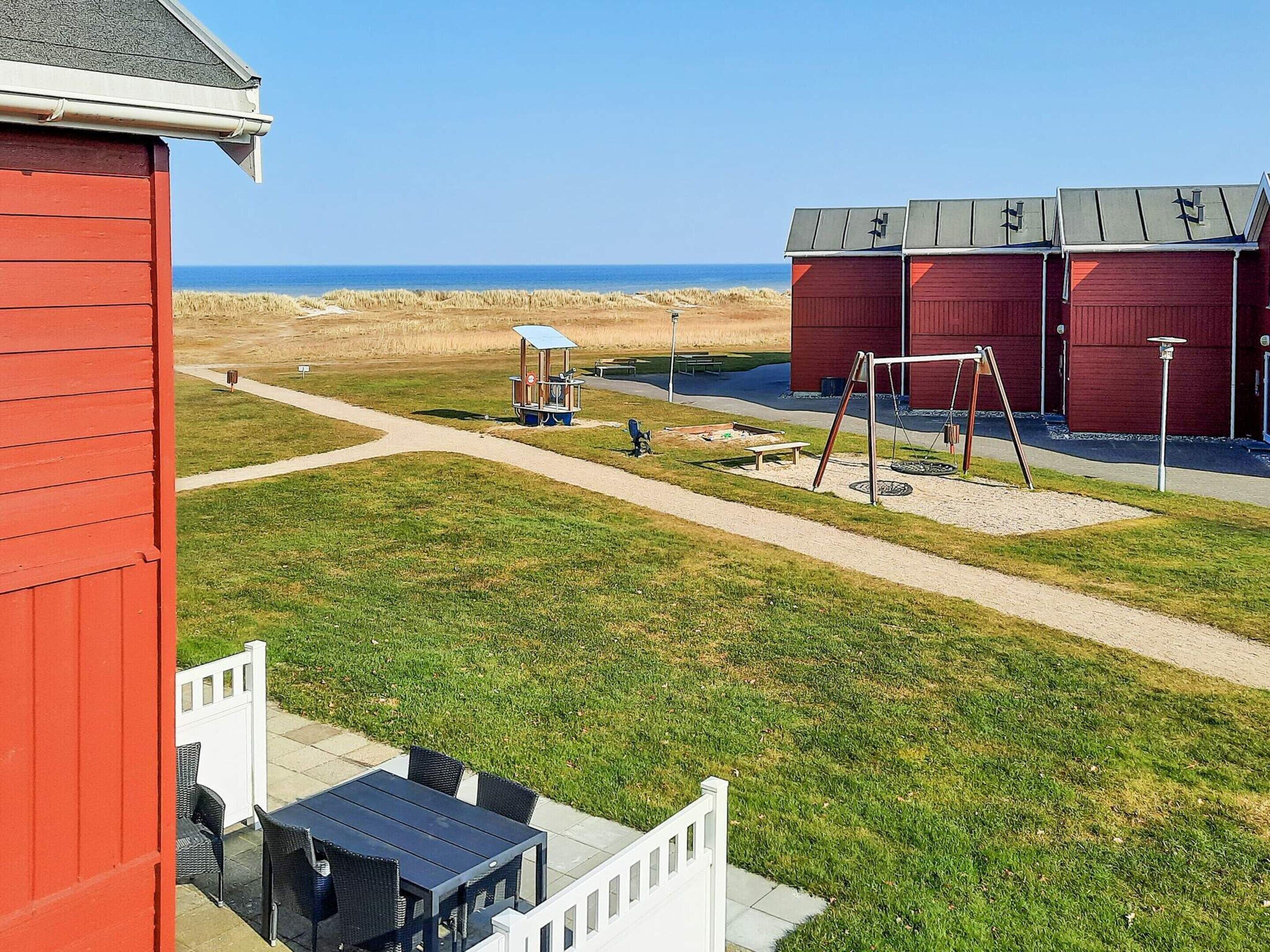 A red building with a white fence, a playground, and a view of the beach.
