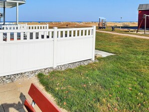 A beachside area with a white fence, a red bench, and a red building with a sloped roof. - 6 Person Holiday Home in Hadsund (Hadsund)