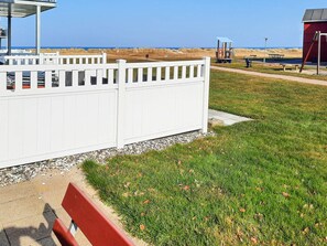 A beachside area with a white fence, a red bench, and a red building.