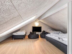 A compact attic bedroom with a sloped ceiling, a flat-screen TV mounted on the wall, and two beds with dark bedding.
