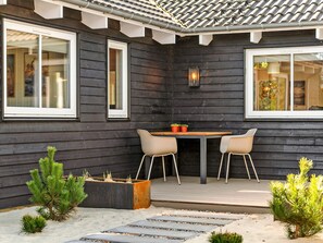 A modern house with a dark exterior, a tiled roof, and a patio area with a table and chairs.