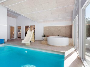 A modern indoor swimming pool with a slide, a large bathtub, and a view of the outside.
