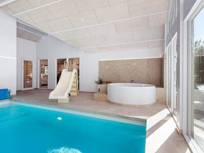 A modern indoor pool area with a slide, a large bathtub, and a view of the outside. - 5 Star Holiday Home in Blavand (Blavand)