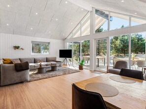 A spacious living room with a large TV, comfortable seating, and a dining area with a view of the outdoors.