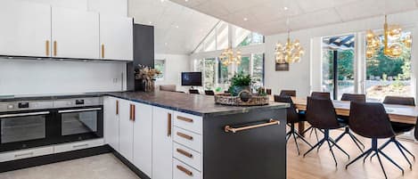 A modern kitchen with a central island, built-in ovens, and a dining area with a large table and chairs.