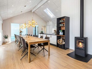 Moderni keittiö, jossa on keskeinen saareke, ruokailutila puupöydällä ja -tuoleilla, sisäänrakennettu liesi ja suuri ikkuna.