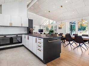 A modern kitchen with a large island, built-in ovens, and a dining area with a view. - 5 Star Holiday Home in Blavand (Blavand)