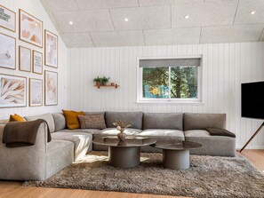 A modern living room with a sectional sofa, two round coffee tables, a large window with a view of trees, and framed artwork on the wall. - 5 Star Holiday Home in Blavand (Blavand)