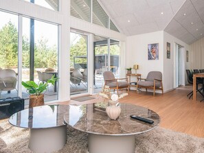 A modern interior with a glass door leading to an outdoor patio, a round marble coffee table, and a dining area with chairs.