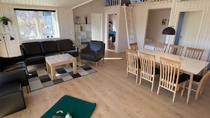 A spacious living area with a black leather sofa, a wooden coffee table, and a dining table with wooden chairs. There is a staircase leading to an upper level. - 8 Person Holiday Home in Vaeggerlose (Vaeggerlose)