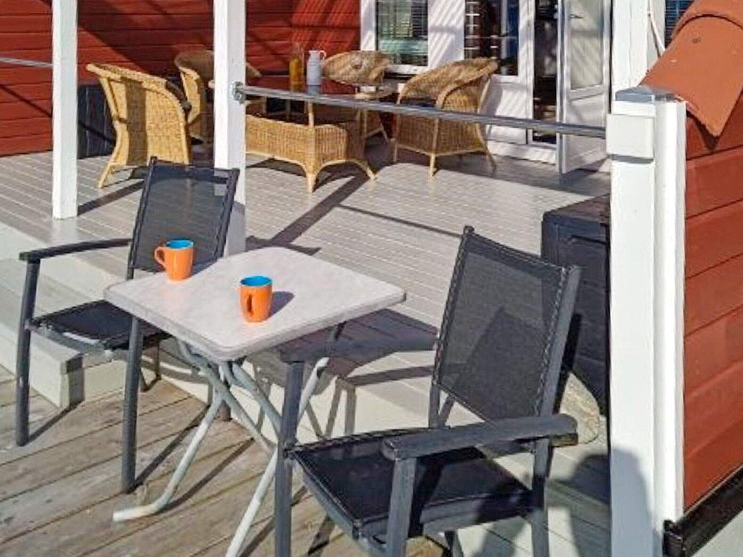 An outdoor seating area with wicker chairs and tables, a wooden deck, and a glass balustrade.