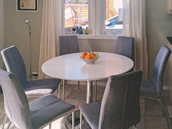 Une table de salle à manger ronde, avec un saladier de fruits au centre, entourée de quatre chaises grises.