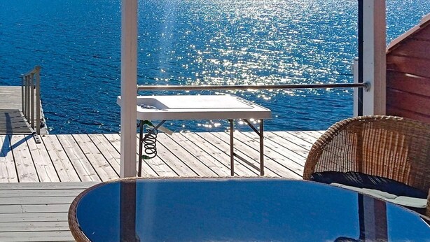 A glass-top table with wicker chairs on a wooden deck overlooking a body of water. - 6 Person Holiday Home in Gursken-by Traum (Sande)