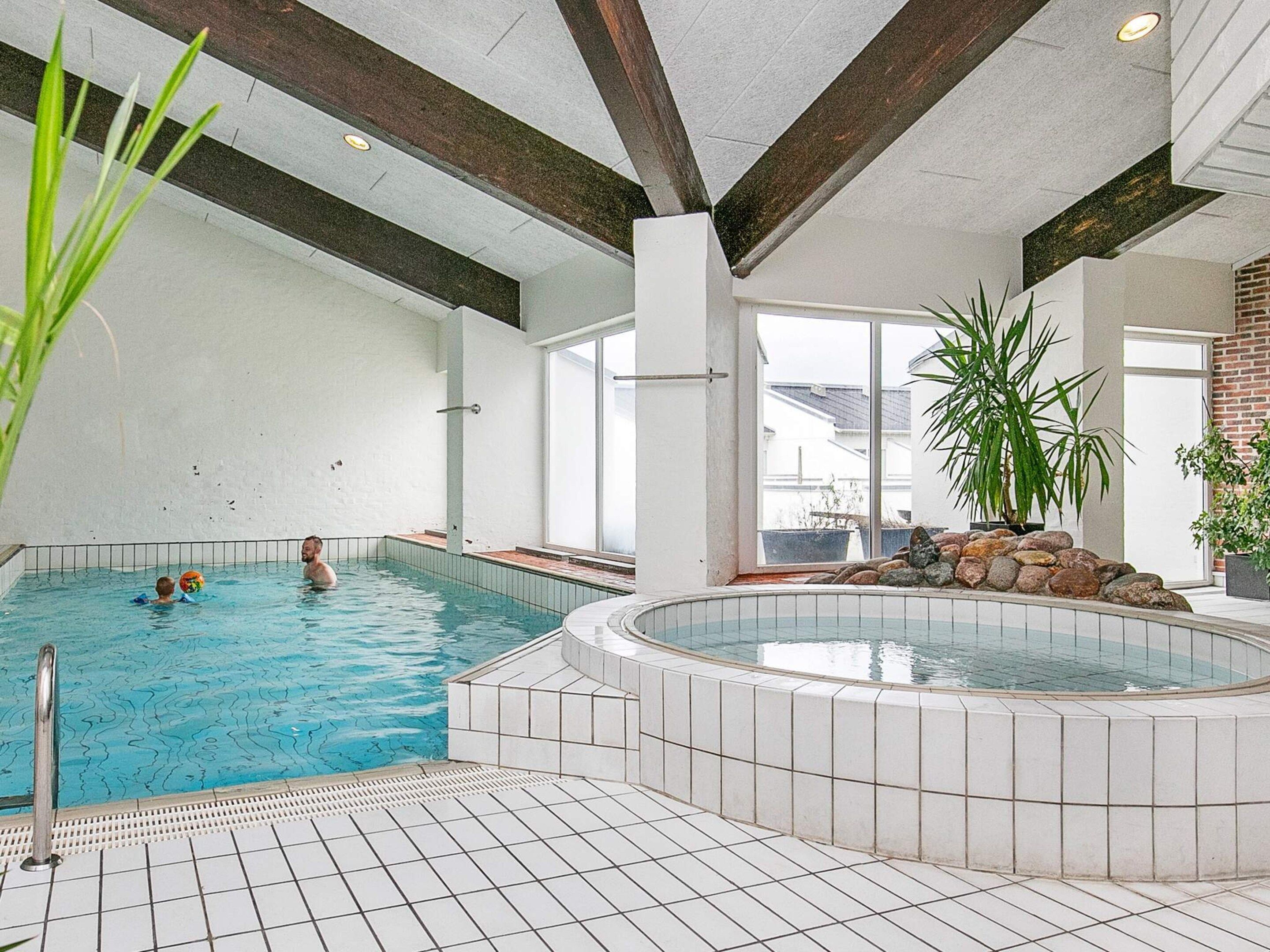 Une piscine intérieure avec un sol carrelé et un espace dédié aux bains à remous.