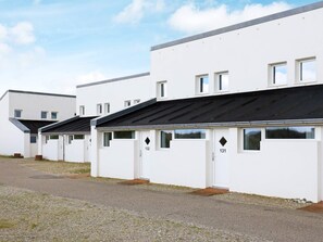 A row of white mobile homes with numbered doors, a gravel driveway, and a clear sky.