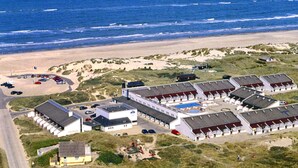 Luchtbeeld van een kusthotel met meerdere gebouwen, een zwembad en een strand op de achtergrond.