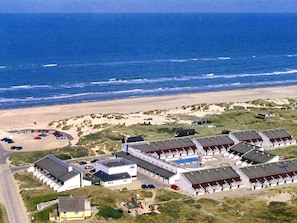 An aerial view of a coastal hotel with multiple buildings, a swimming pool, and a beach in the background.