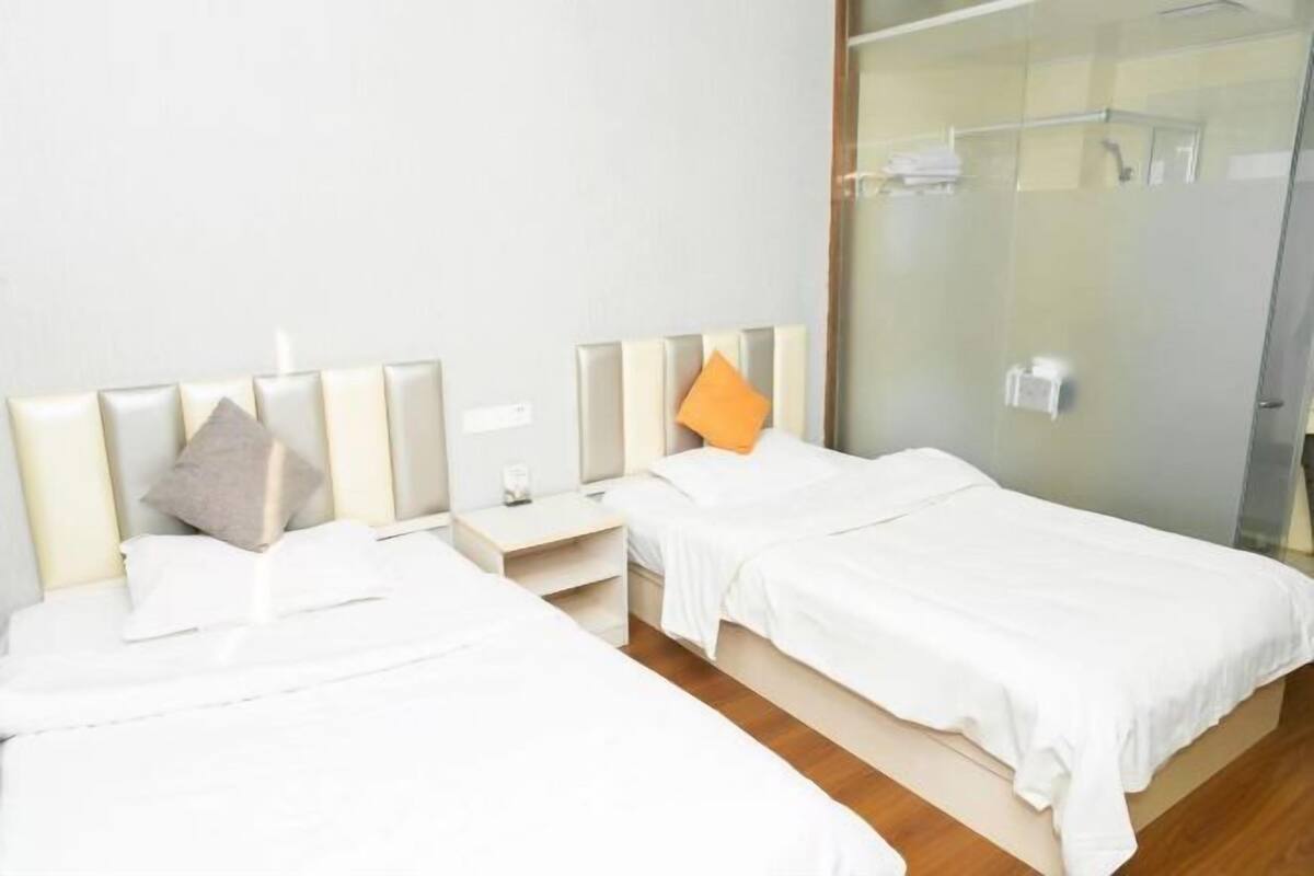 A hotel room with two beds, a glass shower enclosure, and a white color scheme.