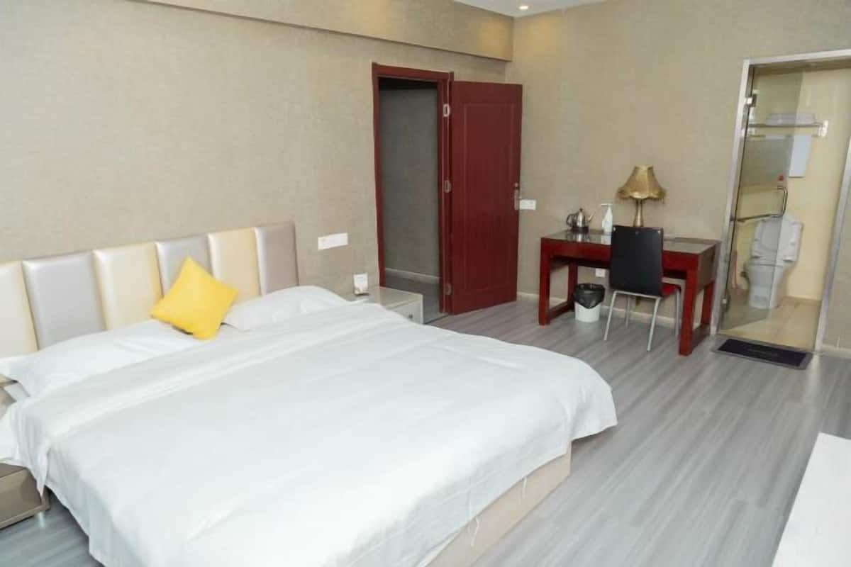 A hotel room with a large bed, a desk, a chair, and a door leading to a bathroom.
