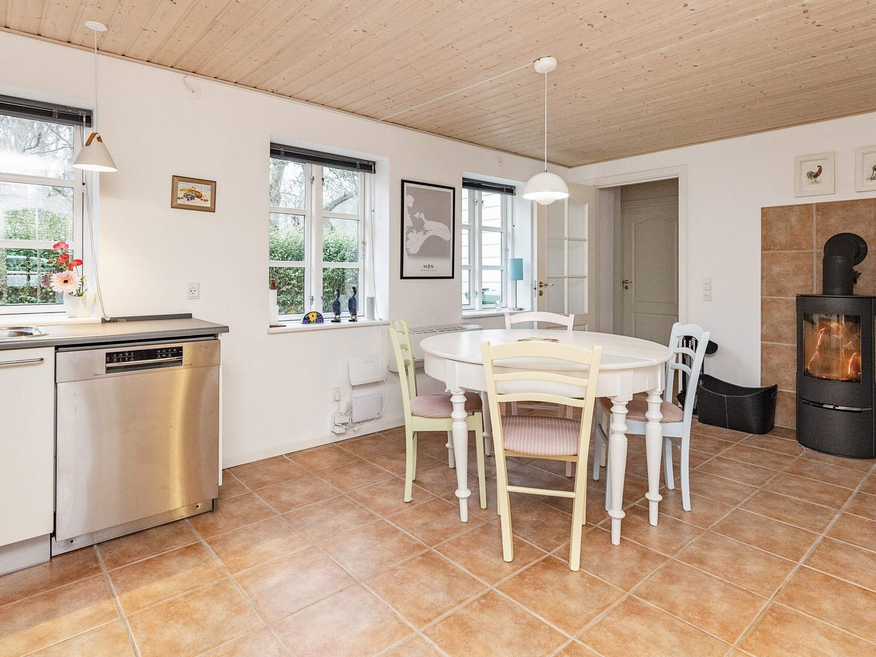A kitchen with a dishwasher, a dining table with chairs, a stove, and a window with a view of greenery.