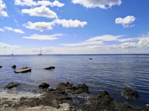 A coastal scene with calm waters, scattered rocks, and a distant sailboat.