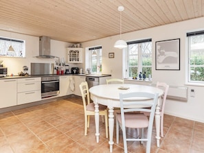 A modern kitchen with white cabinetry, a dining table, and chairs. There are windows with views of greenery outside. - 4 Star Holiday Home in Borre (Borre)