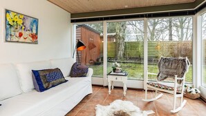 A room with a white sofa, a rug, a rocking chair, and a large window with a view of a backyard. - 4 Star Holiday Home in Borre (Borre)