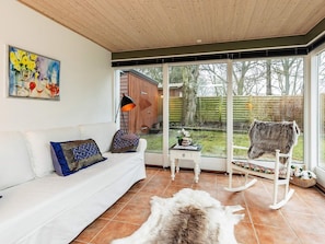 A room with a white sofa, a rug, a rocking chair, and a large window with a view of a backyard. - 4 Star Holiday Home in Borre (Borre)