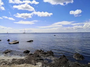 A coastal scene with calm waters, scattered rocks, and a distant sailboat. - 4 Star Holiday Home in Borre (Borre)
