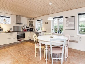 A modern kitchen with white cabinetry, a dining table, and chairs. There are windows with views of greenery outside. - 4 Star Holiday Home in Borre (Borre)
