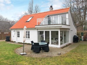 Une maison à deux étages, avec un toit recouvert de tuiles rouges, un balcon et un patio vitré aménagé avec du mobilier d’extérieur.