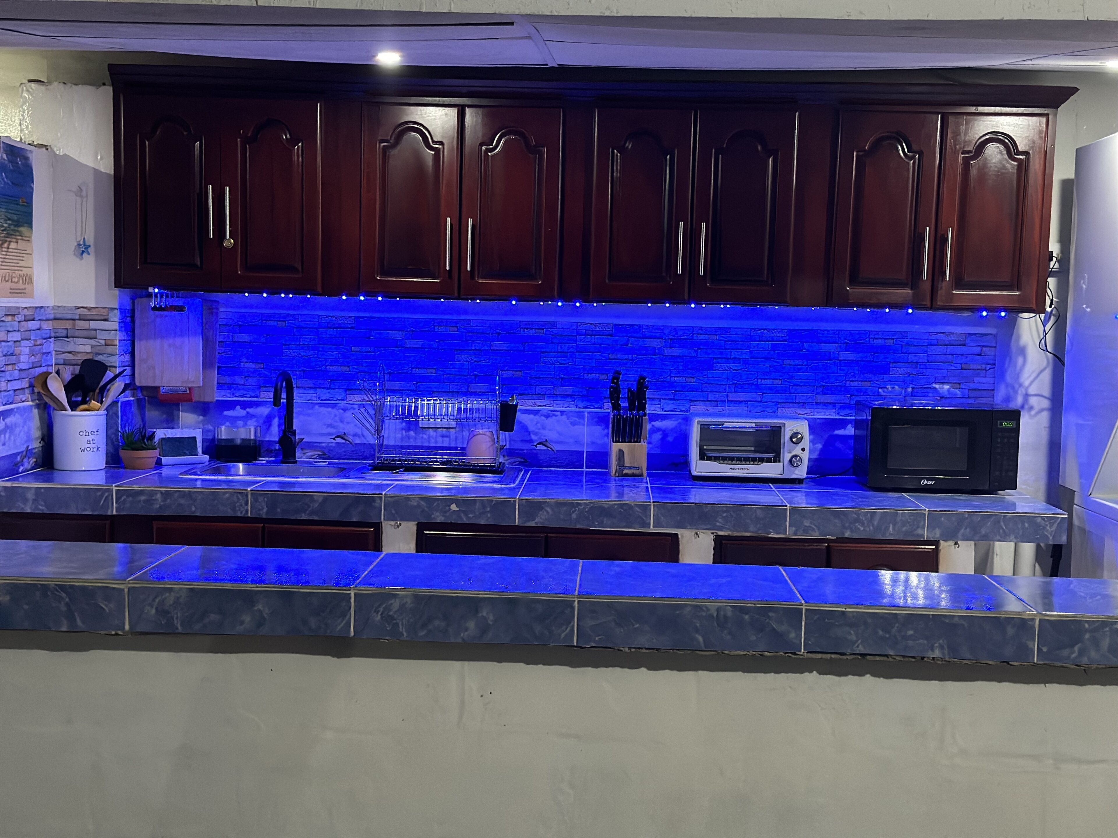Una cocina con armarios de madera oscura, salpicadero azul, microondas integrado y un tostador.