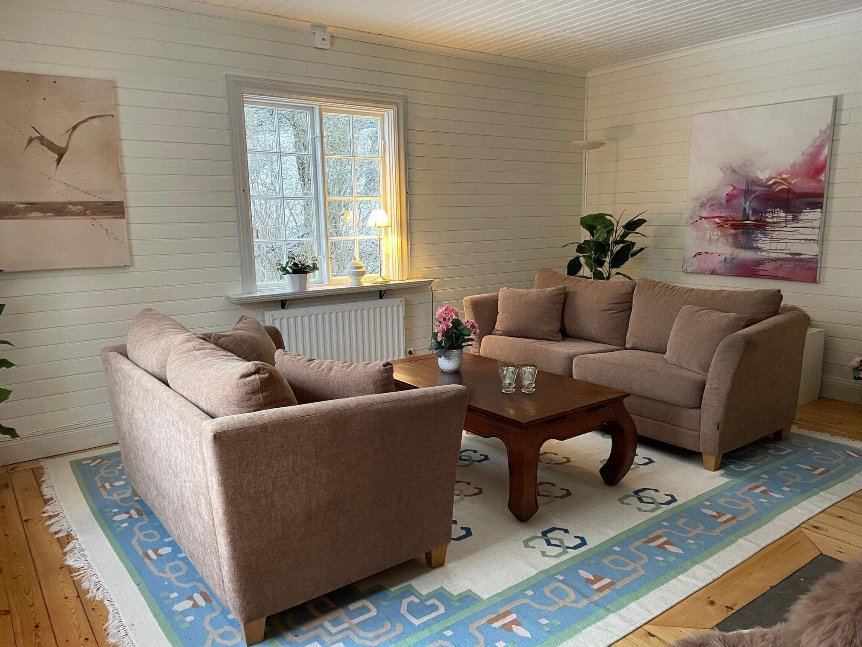 Una sala de estar con un sofá color beige, una mesa de centro de madera y un tapete estampado.