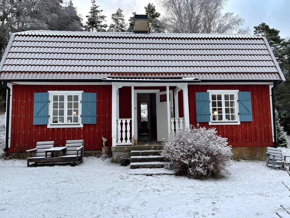 Una casa de madera roja con puerta blanca y contraventanas azules, rodeada de nieve.