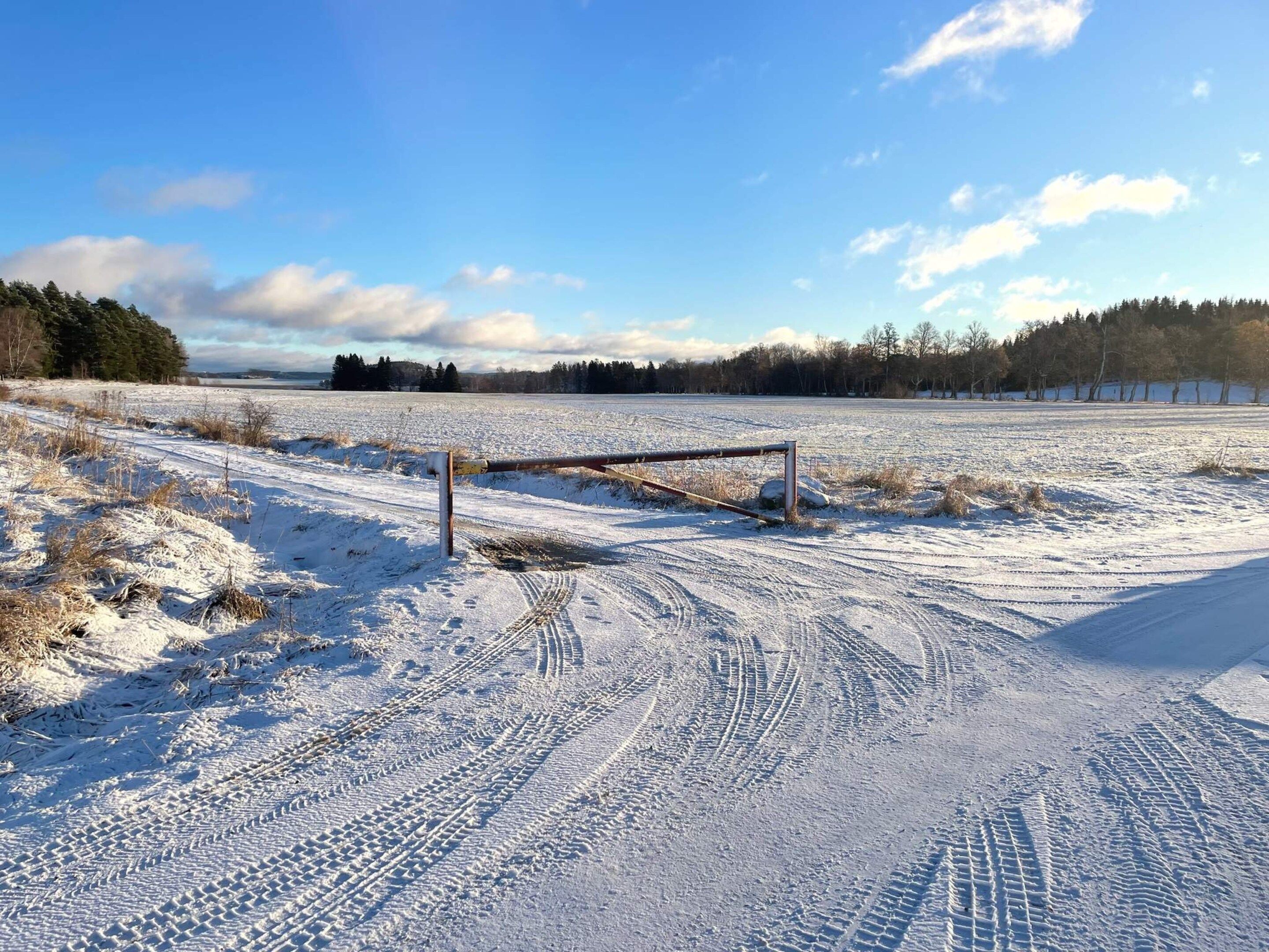 A snow-covered field with a metal gate and tire tracks.