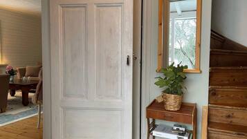 Una habitación con una puerta blanca, una escalera de madera, una pequeña mesa con una planta y un espejo en la pared.