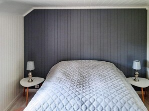 A bedroom with a large bed, two bedside tables with lamps, and a dark headboard.