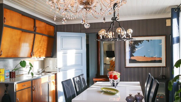 A dining area with a chandelier, wooden cabinets, a white table, and a painting on the wall. - 8 Person Holiday Home in Songe (Tvedestrand)