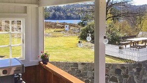A room with a view of a lake and forest, a stone wall, and a wooden bench outside. - 8 Person Holiday Home in Songe (Tvedestrand)